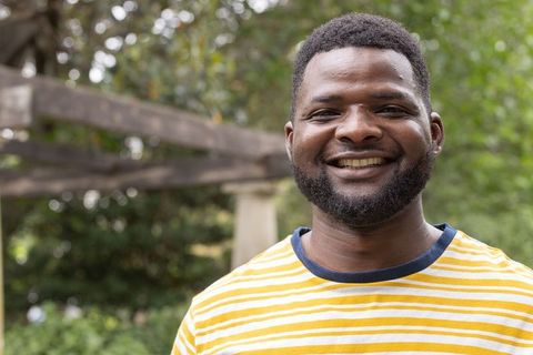 African american man smiling in yellow striped tee, outdoor portrait with wooden pergola
