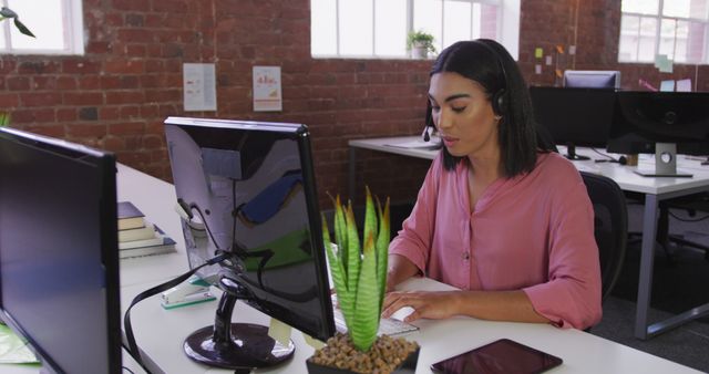 Biracial businesswoman wearing headset sitting at desk having image call. business person at work in modern office