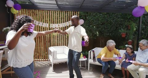 Diverse family dancing and toasting on patio under pergola at birthday celebration