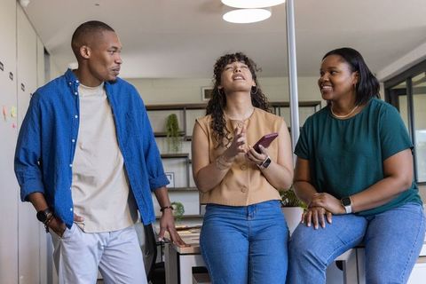 Diverse team collaborating in modern office, sharing smartphone and laughing