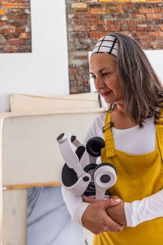 Female artist holding headphones in bright studio surrounded by canvases and brick wall