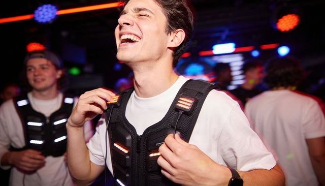 Laughing young man adjusting led vest in neon club nightlife, laser tag party energy
