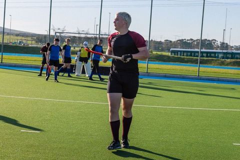 Diverse male field hockey team walking on turf pitch during training