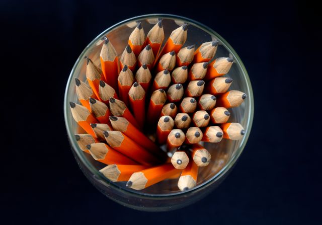 A top view of a group of sharpened orange pencils arranged in a glass against a dark background. Ideal for themes related to education, creativity, office supplies, and back-to-school marketing materials.