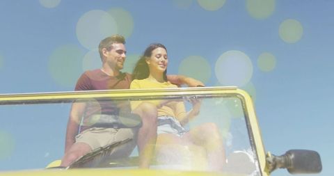 Young couple leaning on convertible windshield enjoying sunny road trip and bokeh light