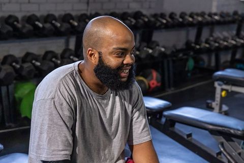 Smiling african american man sitting on bench in gym after strength training session