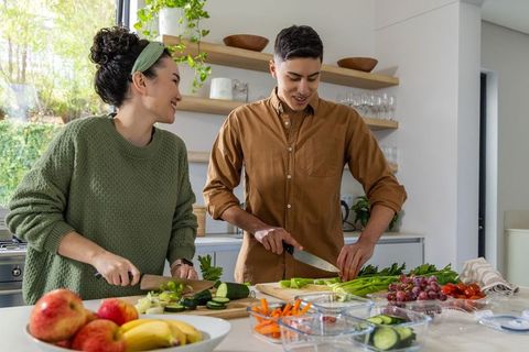 Diverse couple preparing healthy meal together on kitchen island with fresh produce