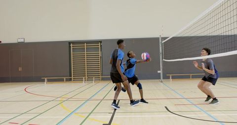 High school athletes lunging and passing volleyball in indoor gym during team practice