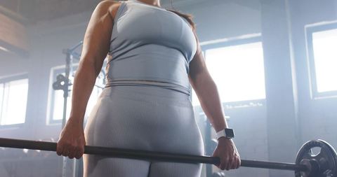 Mid-adult female lifting and gripping loaded barbell in industrial gym