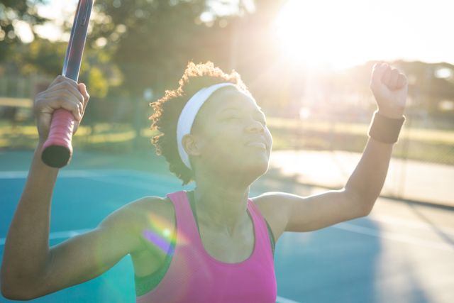 Young African American female tennis player celebrating a win on the court. Ideal for use in sports promotions, fitness campaigns, motivational materials, and advertisements highlighting success and active lifestyles.