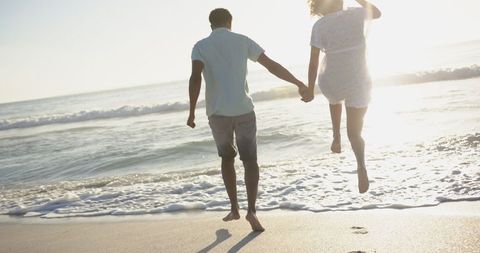 Romantic couple on sunlit summer beach walking hand in hand