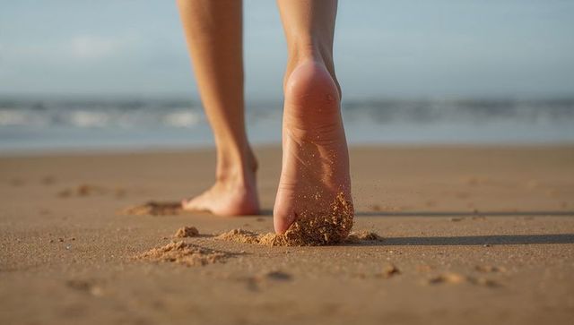 Bare feet walking on wet sand leaving footprints at golden hour by ocean horizon