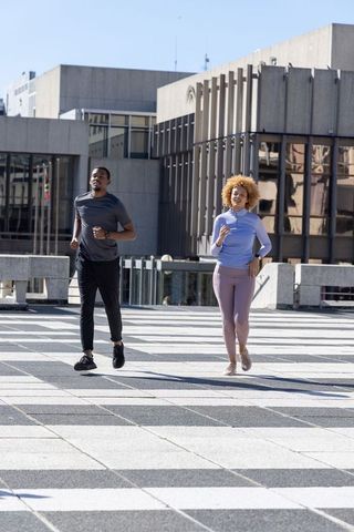 African American Couple Jogging on Urban Plaza with Modernist Architecture and Sunlight