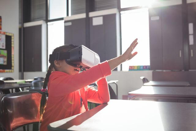 Girl gesturing while using virtual reality glasses in classroom at school