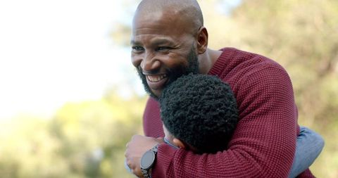African american father embracing son in sunlit park smiling showing warm family bond