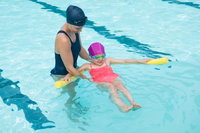 Female instructor training young girl in pool at leisure center