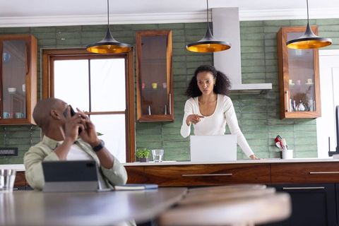 Black couple discussing remote work in modern kitchen with laptop and smartphone