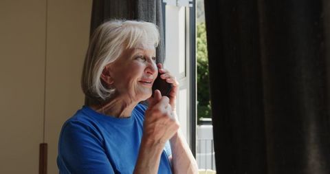 Senior woman using smartphone near window in bright room
