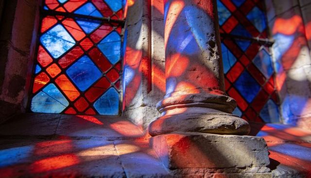 Colored stained glass light bathing weathered stone column base in gothic chapel window