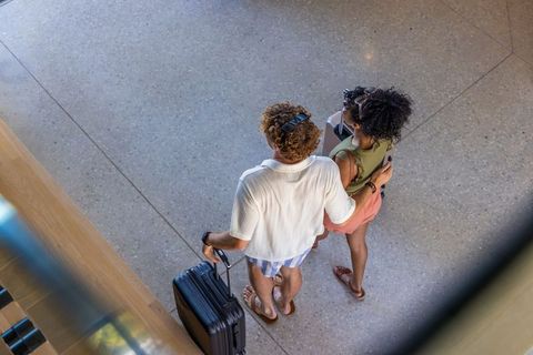 Aerial view of diverse couple walking through airport concourse pulling suitcase from above