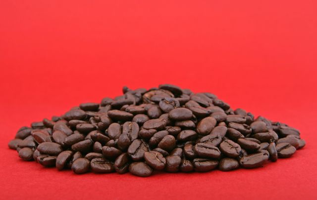 Heap of roasted coffee beans on red background is perfect for advertising coffee products, coffee shops, and restaurants. Also ideal for websites, posters, and packaging that focus on coffee-related themes, providing a sense of freshness and quality.