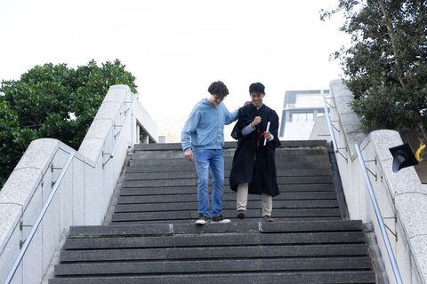 Friends celebrating graduation walking down campus steps graduate holding diploma