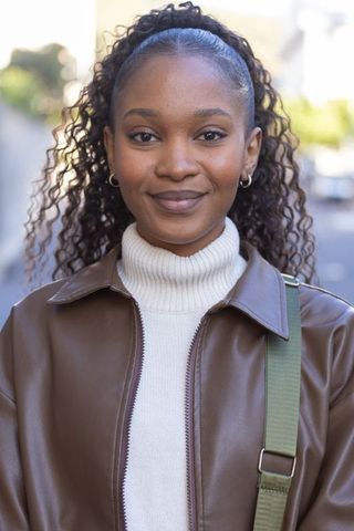 Smiling african american woman wearing turtleneck leather jacket on sunlit city street
