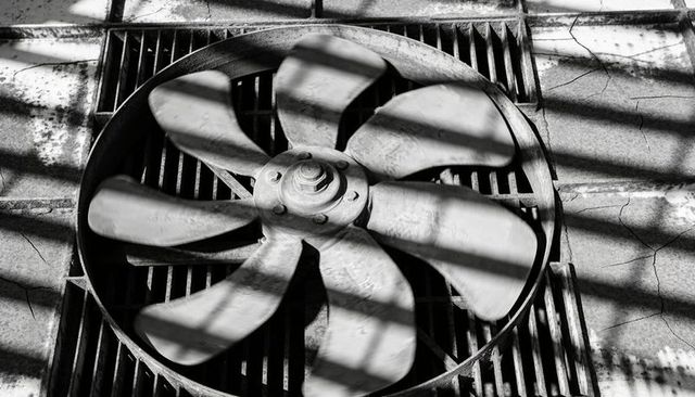 Weathered rooftop ventilation fan with dramatic shadow bands and industrial texture