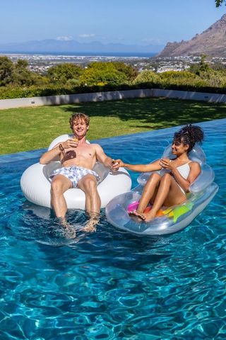 Diverse couple relaxing on inflatable floats in luxury infinity pool with ocean view
