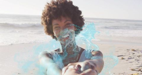 Smiling Black woman holding partner's hands on sunlit beach with joyful blue splash overlay