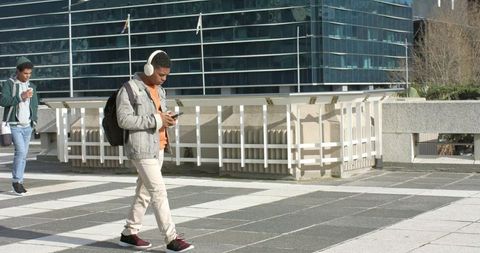 African american men walking urban plaza wearing headphones and using smartphone