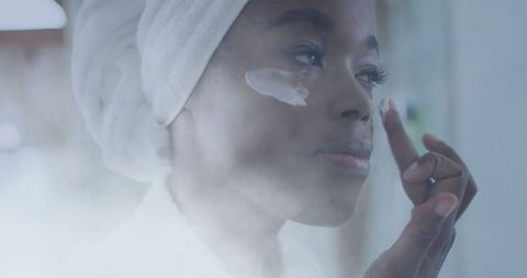 African american woman applying facial cream in relaxing atmosphere