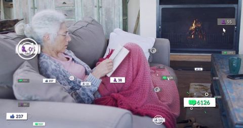 Senior woman reading on sofa with pink throw and social media ui overlays by fireplace