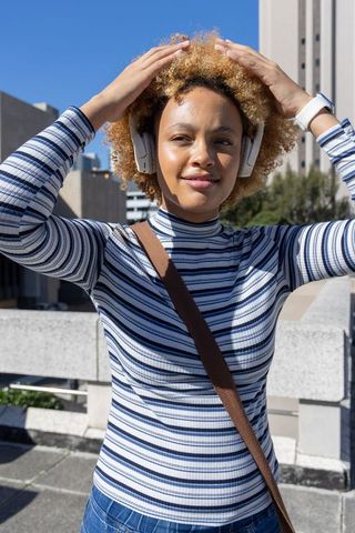 Young african american woman adjusting headphones on urban rooftop terrace wearing smartwatch