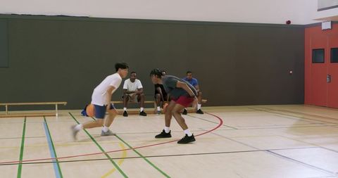 Asian guard performing crossover dribble while black defender sliding low during drill