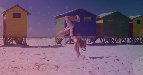 Playful Girl Handstands on Sunny Beach Near Colorful Cabins