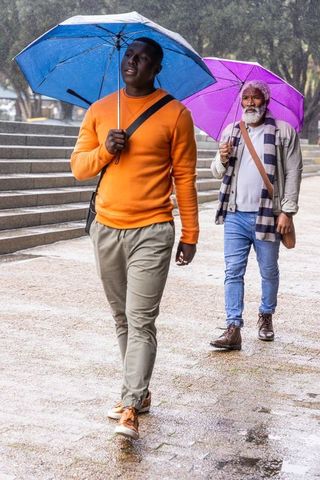 African american men walking in rain with colorful umbrellas on urban plaza