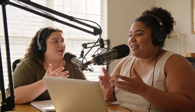 Recording friendly podcast cohosts speaking into microphones in bright home studio