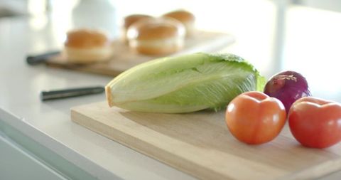 Sunlit countertop romaine lettuce and ripe tomatoes with red onion on cutting board