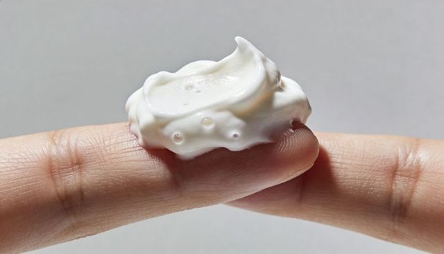 Fingertip holding dollop of white cream on finger, macro closeup showing skin texture