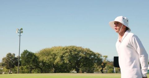 Man standing in profile on sports field wearing white bucket hat enjoying sunny weather