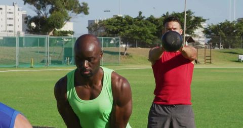 Men Engaged in Outdoor Kettlebell Training on Green Field