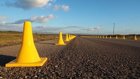 Leading yellow traffic cones lining rural paved road into distant horizon at golden hour