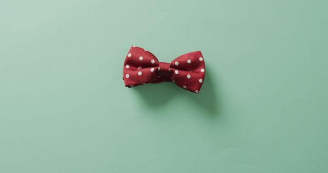 Red polka dot bow tie lying on light green background. Perfect for use in marketing fashion accessories, branding for men's clothing lines, or articles discussing trends in menswear. It can also be used for invitations, greeting cards, and other stylish creative projects.
