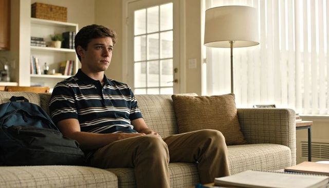 Teen student sitting on couch gazing thoughtfully with backpack at home living room calm