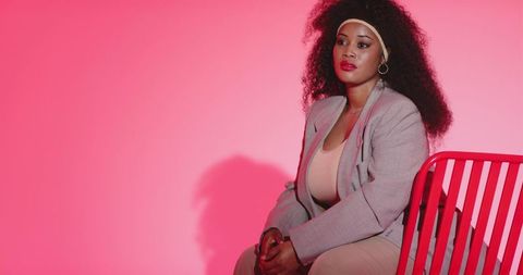 African-american woman posing on pink backdrop wearing blazer and hoop earrings, glamorous fashion p