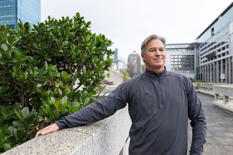 Senior man leaning on concrete railing on urban rooftop terrace with greenery and city view
