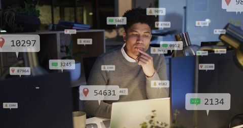 Late-night office worker monitoring notifications and data on laptop and monitors