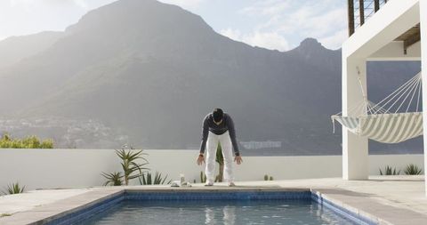 Indian man practicing morning yoga on modern poolside terrace with mountain view