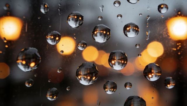 Rain droplets refracting urban lamp lights at dusk with warm bokeh reflections